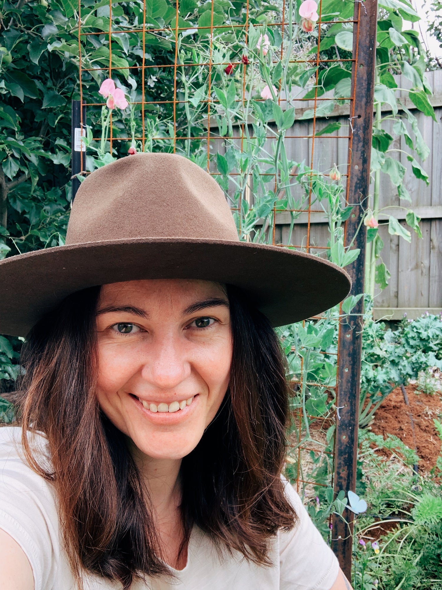 A photo of Vic wearing a brown felt hat and smiling into the camera in her former tiny urban vegetable garden